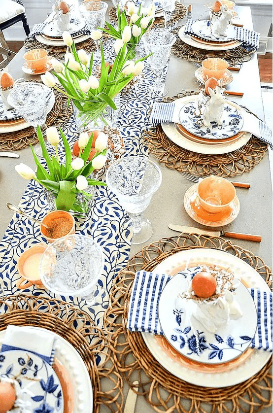 a bright, rustic Easter tablescape with printed linens, rattan shutters, white tulips, candles and eggs, and floral plates