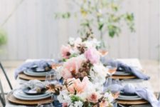 a bright spring table setting with navy napkins and a table runner, wicker chargers and blue porcelain and pink and white floral centerpieces