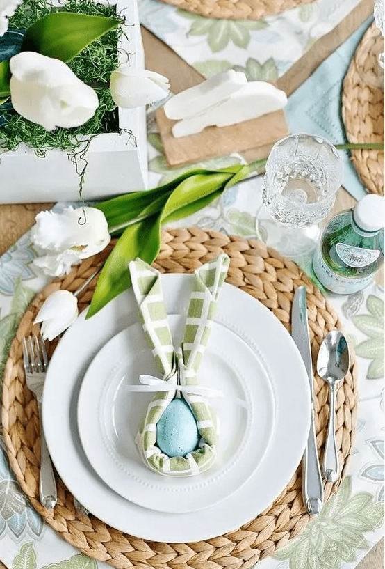 a chic Easter table setting with botanical placemats, woven chargers, pastel napkins, white tulips and eggs