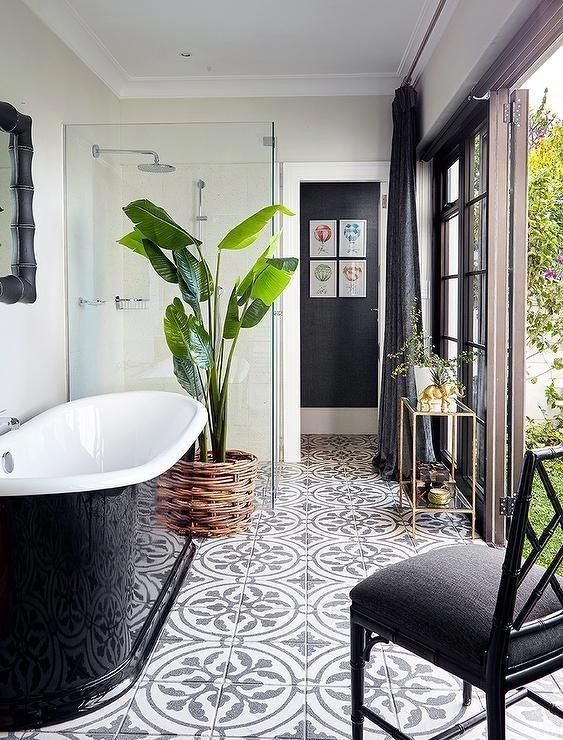 a chic monochromatic bathroom with a tile floor, a black tub and chair and a statement plant ina  wicker pot