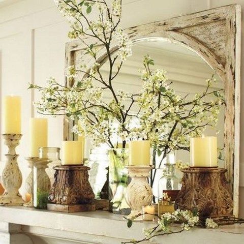 a chic spring mantel with blooming branches, candles on stands and in candle holders, a large mirror on the mantel
