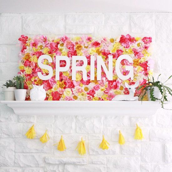 a colorful spring mantel with a yellow tassel garland, potted greenery and a fake bloom sign with letters