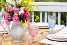 a colorful spring tablescape with bright glasses, a bright floral centerpiece, woven placemats and a runner