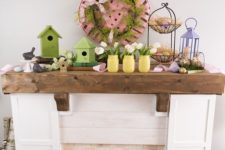 a cozy Easter mantel with green bird houses, yellow jars with blush tulips, faux eggs and nests and a pink basket with greenery