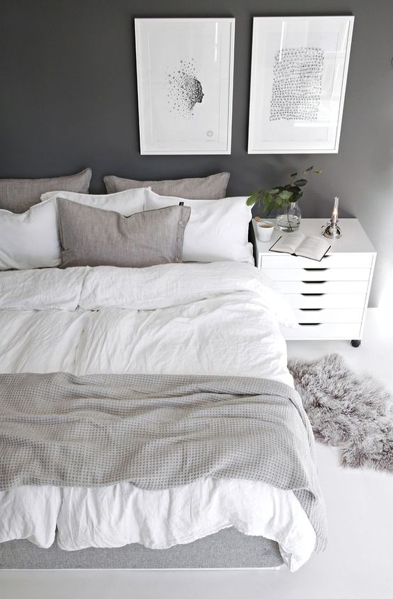 a cozy Scandinavian bedroom with a black statement wall, a bed with greish bedding, a white nightstand and artworks