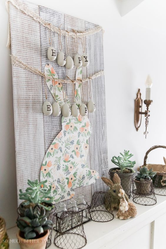 a cute Easter mantel with a large bunny sign with eggs and letters, some bunny figurines and wire planters and succulents