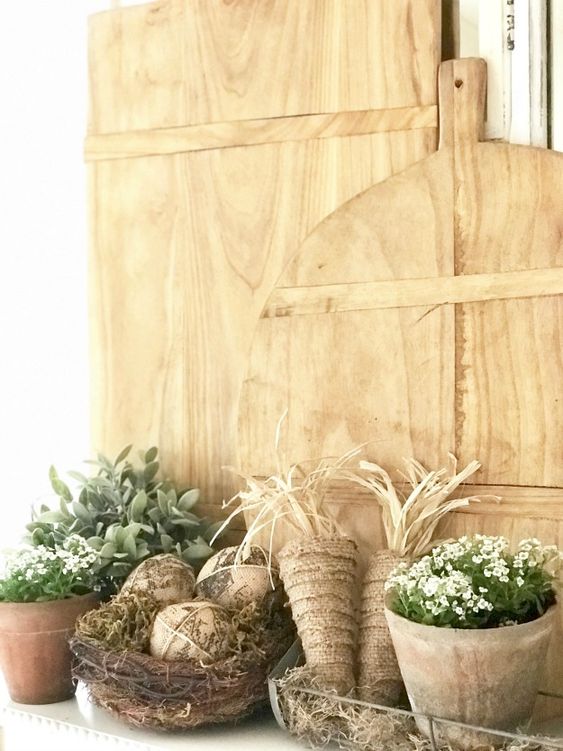 a farmhouse Easter mantel with cutting boards, burlap carrots, fake eggs in a nest and potted blooms