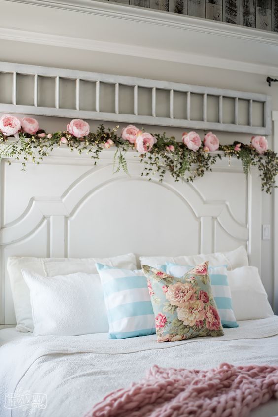 a floral pillow, a pink blanket and a garland of faux greenery and pink peonies make the bedroom feel like spring