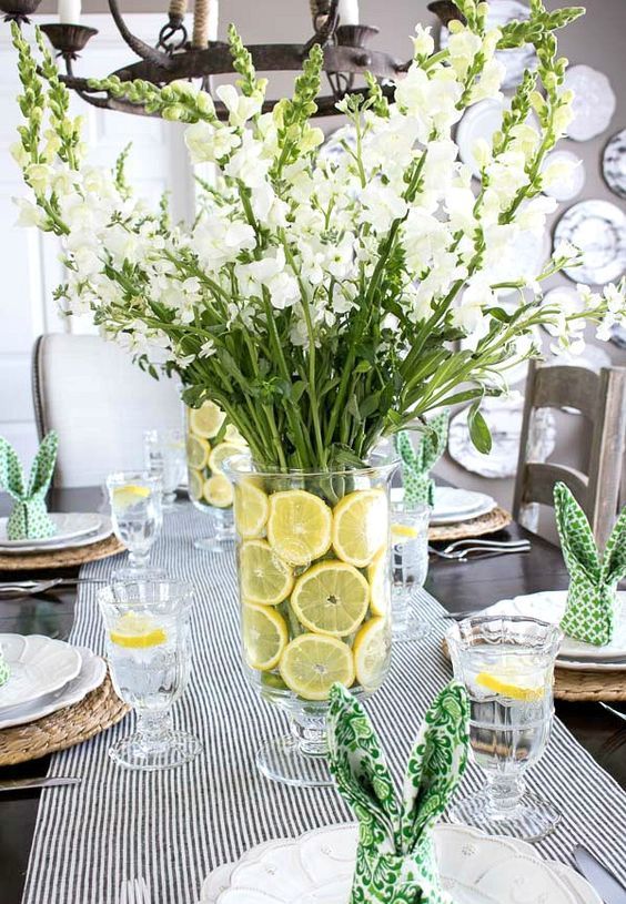 a fresh modern spring tablescape with a white floral centerpiece with lemon slices, wicker chargers, printed bunny napkins