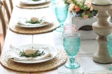 a fresh spring table with wicker chargers, blue and pink glasses, little eggs and greenery plus a lush centerpiece