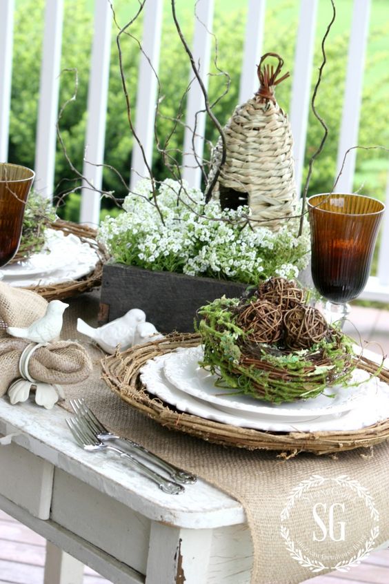 a lovely rustic Easter tablescape with burlap napkins and runners, woven placemats, nests with greenery, blooms and twigs is lovely
