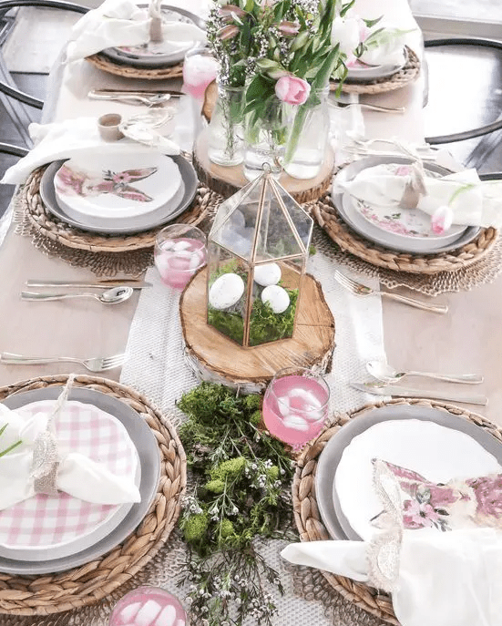a lovely rustic Easter tablescape with woven placemats, greenery, moss, plaid plates, terrariums with moss and eggs and pink tulips