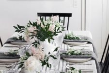 a modern spring tablescape with white and blush blooms and greenery, grey napkins, a striped runner and cool glasses