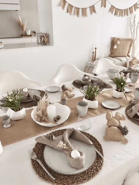 a neutral Easter tablescape with a burlap runner, woven chargers, neutral linens, burlap bunners, potted blooms and candles