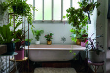 a pretty moody bathroom with a pink tub, colorful planters with greenery all around and a brick wall for interest