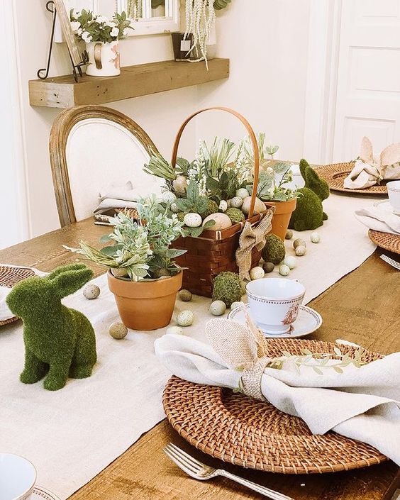a pretty rustic Easter tablescape with a wooden basket with eggs, blooms and moss, fake eggs, moss bunnies and woven placemats is cool