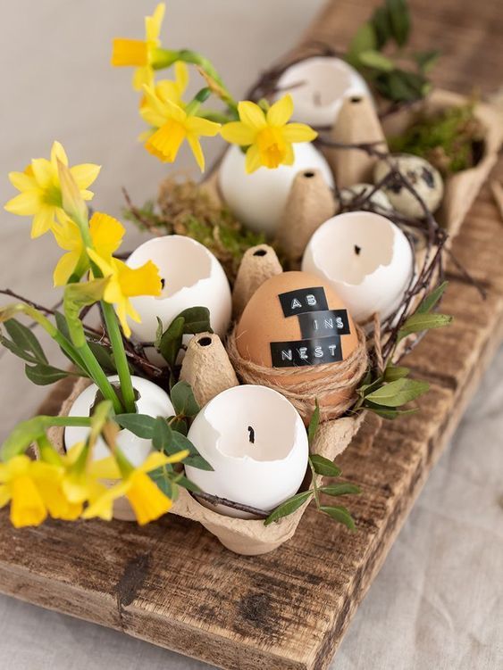 a rustic Easter centerpiece of an egg carton with egg shell candles and bright yellow blooms is a cool solution