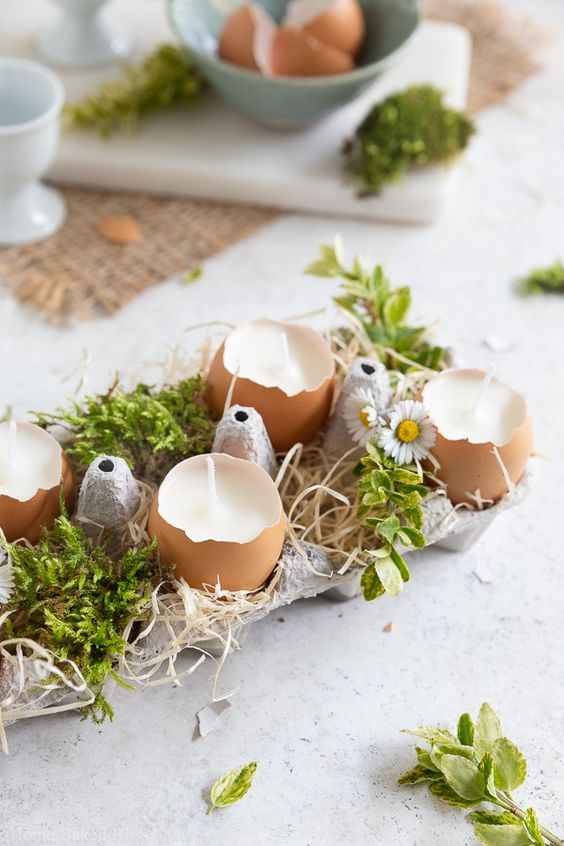 a rustic Easter centerpiece of an egg carton with egg shell candles and moss and blooms is a cool idea
