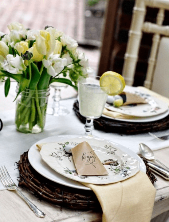 a rustic Easter table with a white and yellow tulip centerpiece, vine placemats printed porcelain and chic cutlery and elegant glasses