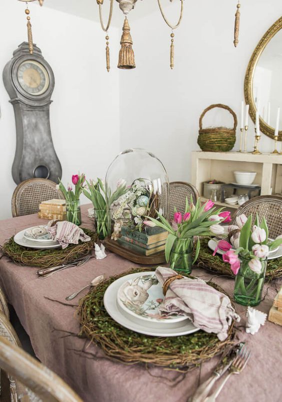 a rustic Easter tablescape with an egg cloche, vine and moss placemats, pink and white tulips and greenery and books stacked is wow