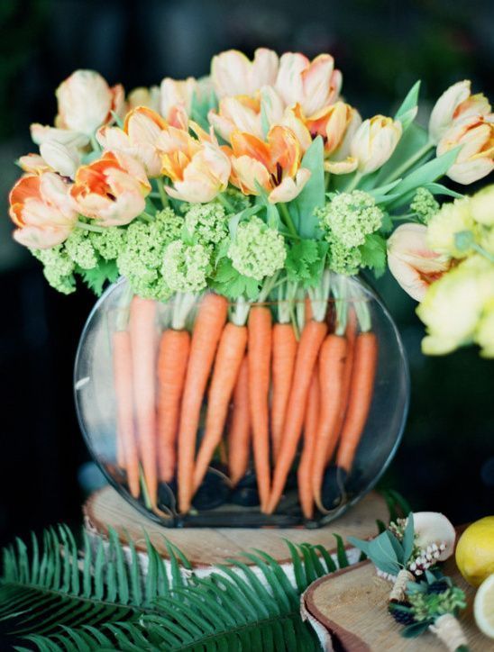 a simple Easter arrangement of carrots, greeneyr and orange tulips in a large rounded vase