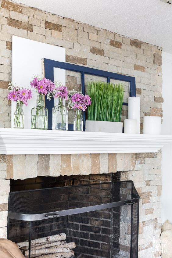 a simple spring mantel with grass in a pot, pillar candles and some pink floral arrangements in clear vases