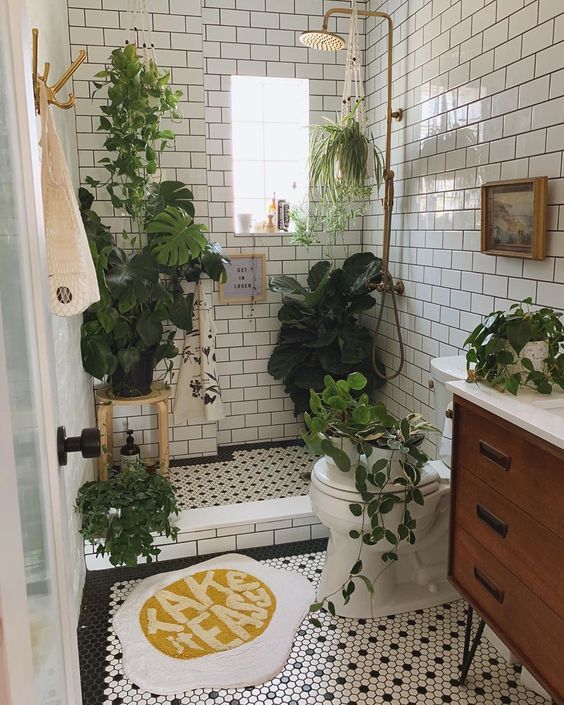 a small and neutral bathroom with a wooden vanity, lots of greenery in pots and some suspended plants