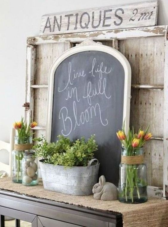 a vintage farmhouse mantel with tulips in clear vases, potted greenery, fake eggs and a rabbit