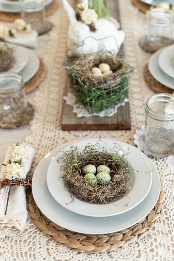 a vintage rustic Easter tablescape with doily runners, nests with eggs for decor, neutral napkins and jars instead of glasses