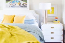 bright blue and sunny yellow bedding for a contrast and bold artworks make the space spring-summer-infused