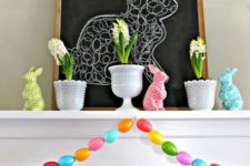 colorful easter mantel styling with a colorful egg garland, colorful bunny figurines and spring bulbs in pots