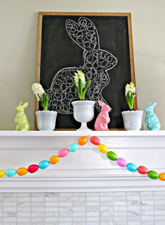 colorful easter mantel styling with a colorful egg garland, colorful bunny figurines and spring bulbs in pots