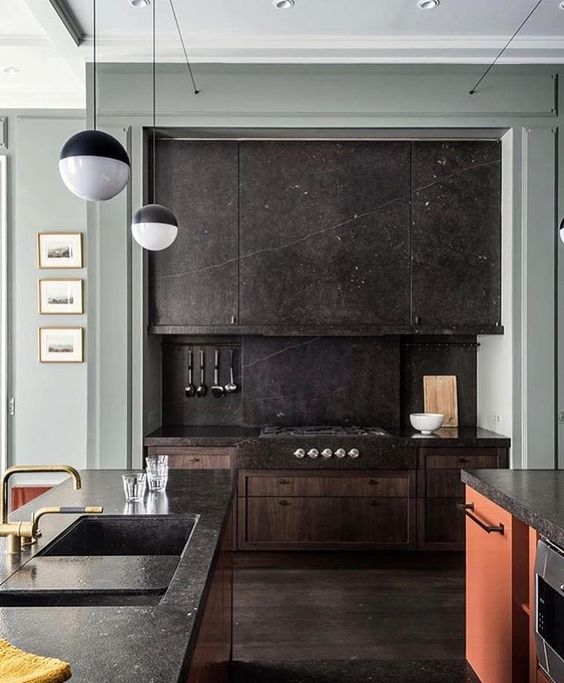 a black stone kitchen with a backsplash, a colorful kitchen island with a stone countertop and pendant lamps