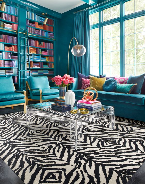 a bold and chic blue living room with bookcases, blue seating furniture, an acrylic table and a zebra print rug and touches of gold