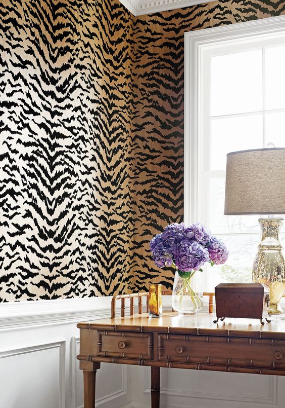 a bold and pretty space with tan and black tiger print wallpaper, white paneling, a vintage colonial-style table, a chic lamp and purple blooms
