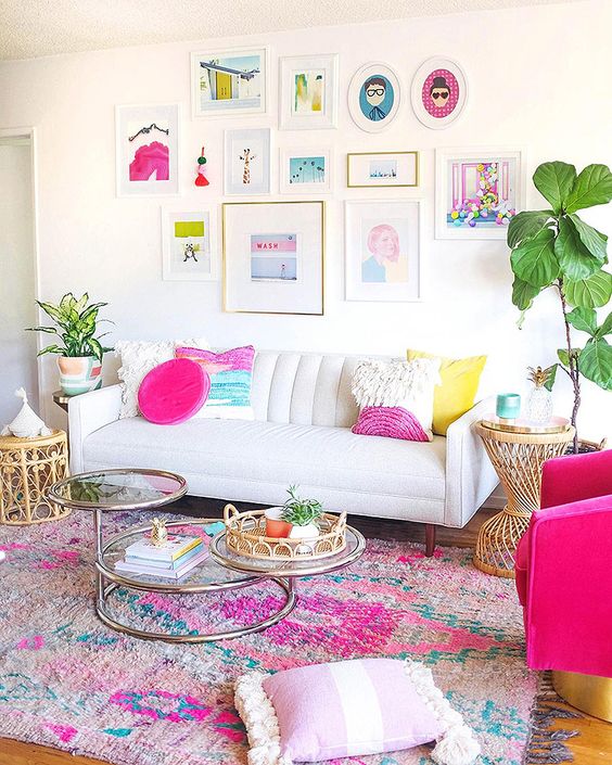 a bright and fun feminine living room with a white sofa, a hot pink chair, a colorful rug, a tiered coffee table, colorful pillows and a bold gallery wall