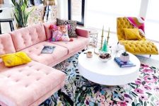a bright girlish living room with a colorful floral print rug, a pink sofa, a mustard lounger, colorful pillows and potted greenery