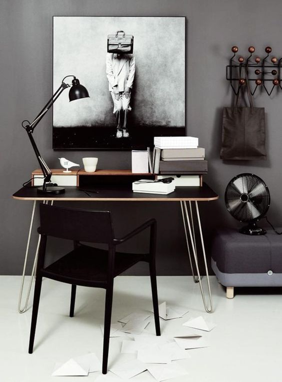a catchy home office with cocnrete walls, a black deks with hairpinlegs, a black chair and catchy decor