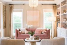 a chic and modern living room with neutral built-in furniture, neutral chairs and a pink sofa, a round table and a beaded chandelier is cool