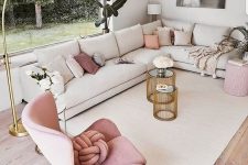 a chic contemporary living room with a feminine feel, a large corner sofa, a blush rocker and a pouf, pink pillows and a gold floor lamp