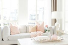 a chic light-filled living room with a grey sofa, peachy pink pillows, a marble slab coffee table and touches of pink