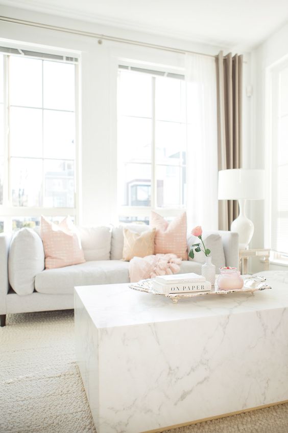 a chic light-filled living room with a grey sofa, peachy pink pillows, a marble slab coffee table and touches of pink