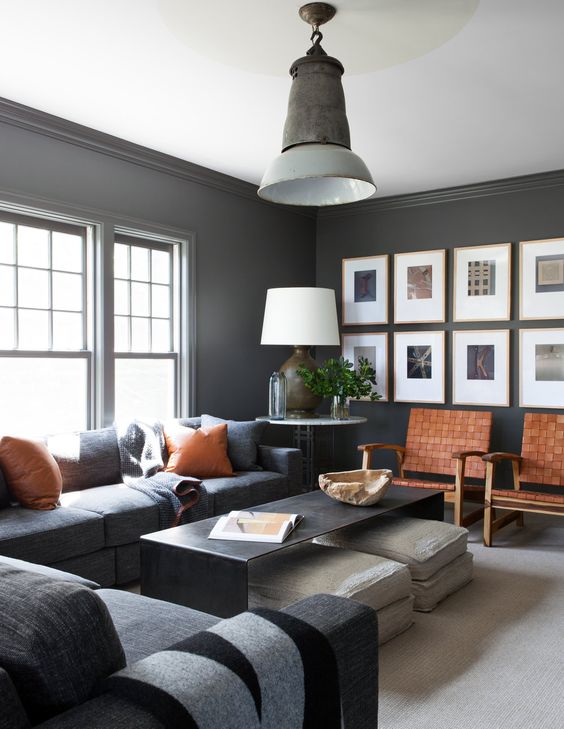 a chic masculine living room with dark furniture and walls, amber leather touches and chairs, some cushions and a coffee table