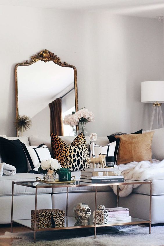 a chic neutral living room with a white sectional, printed pillows including a leopard print one, a glass coffee table with a leopard print box