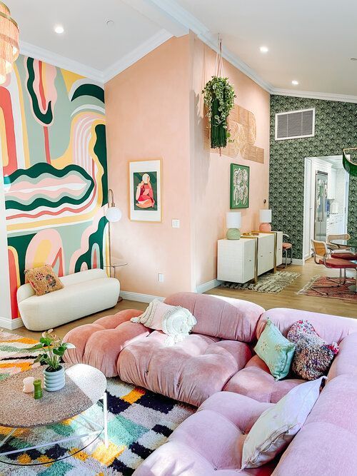 a colorful feminine living room with peachy walls, a statement colorful wall, a lilac low sofa, a colorful rug and a color block table