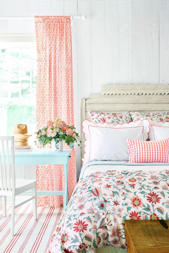 a colorful vintage bedroom with elegant vintage furniture, floral bedding, printed curtains, a blue table and bold blooms