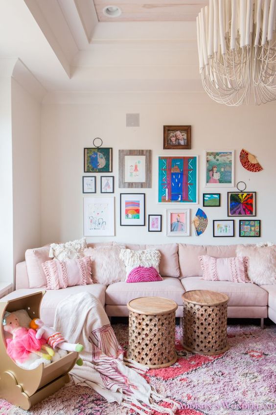 a feminine living room with neutral walls, a light pink sofa with fringe pillows, a colorful gallery wall, Moroccan stools and a pink rug