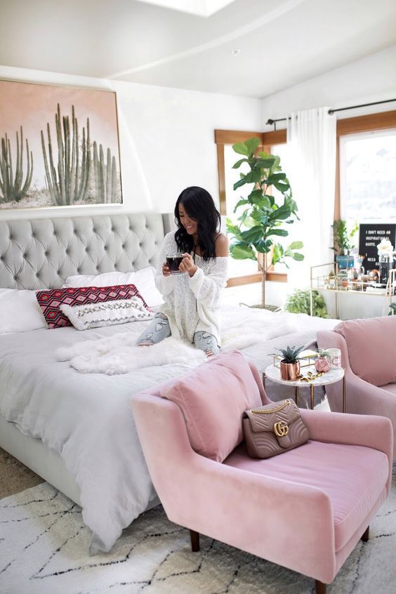 a fun feminine bedroom with a large grey bed, pink chairs, statement plants, a cactus artwork and boho pillows