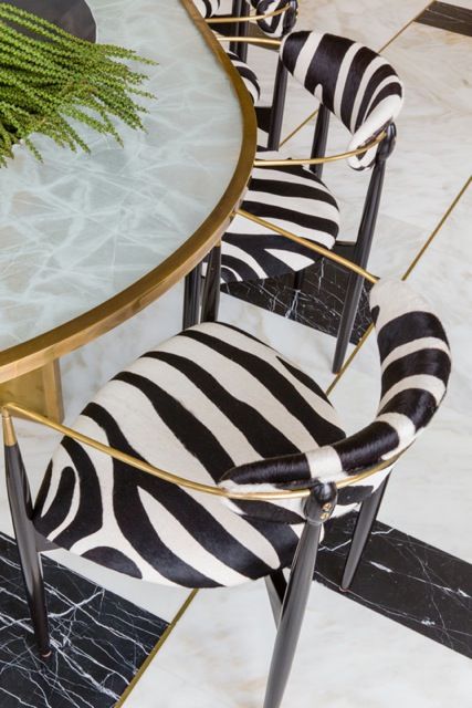 a glam and chic space wiht a marble table with a gold edge, zebra printed chairs with gold frames that echo with the black and white floor