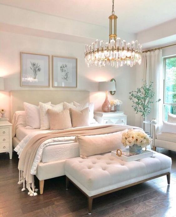 a glam and feminine bedroom with neutral furniture, a statement crystal chandelier, botanical artworks and real blooms